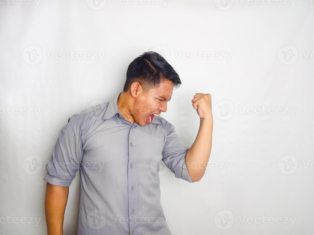 Young Asian man screaming success with his fist clenched wearing grey shirt isolated on white background photo