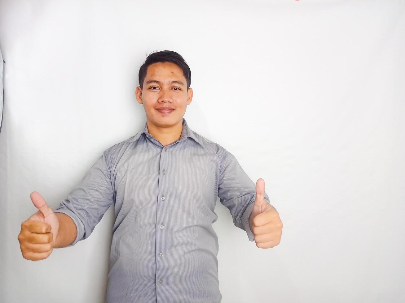 Adult Asian man smiling happy while pointing and give OK sign. wearing grey shirt isolated on white background photo