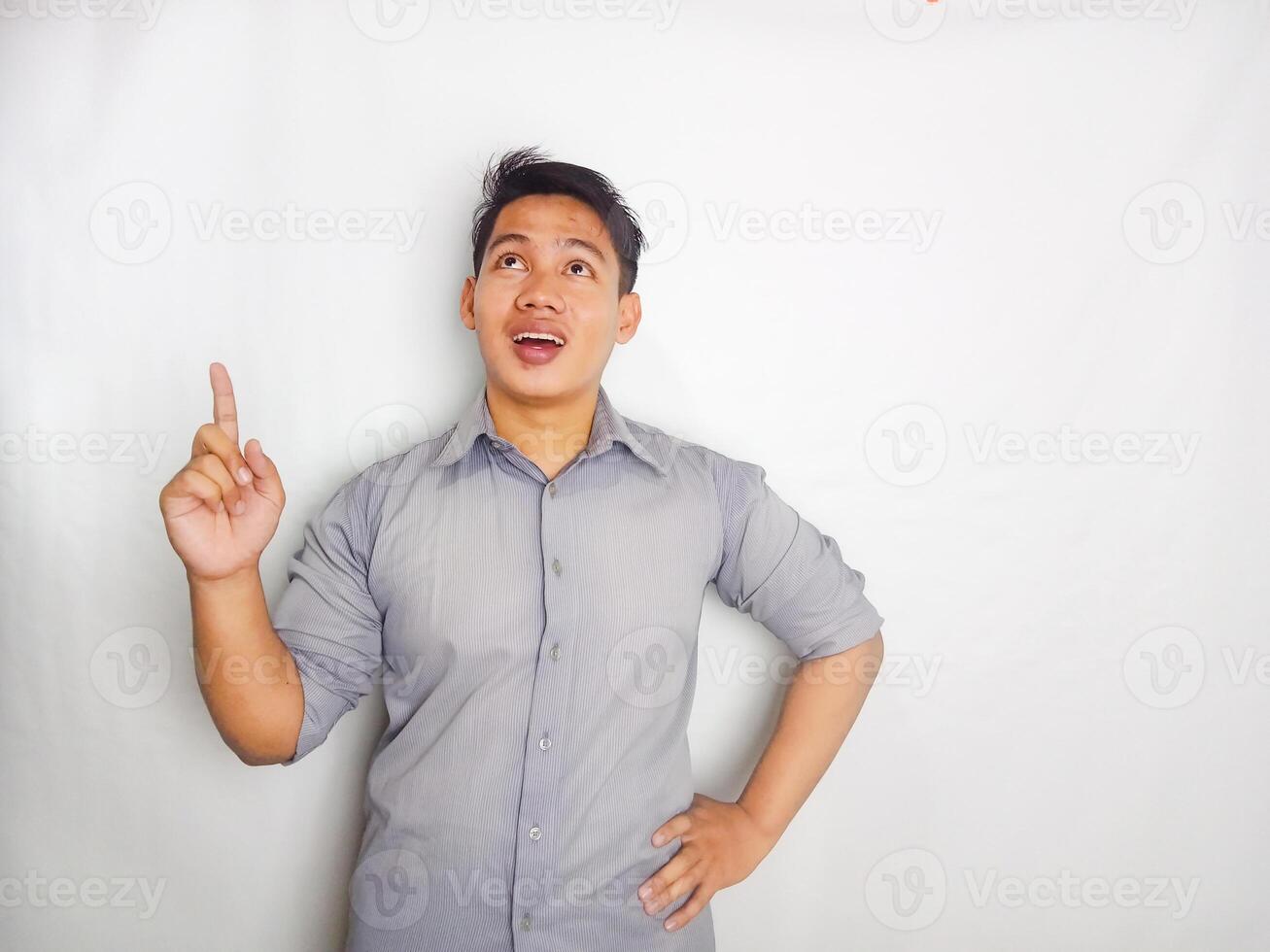 Attractive Young Asian man smiling while pointing to copy space area wearing grey shirt isolated on white background photo
