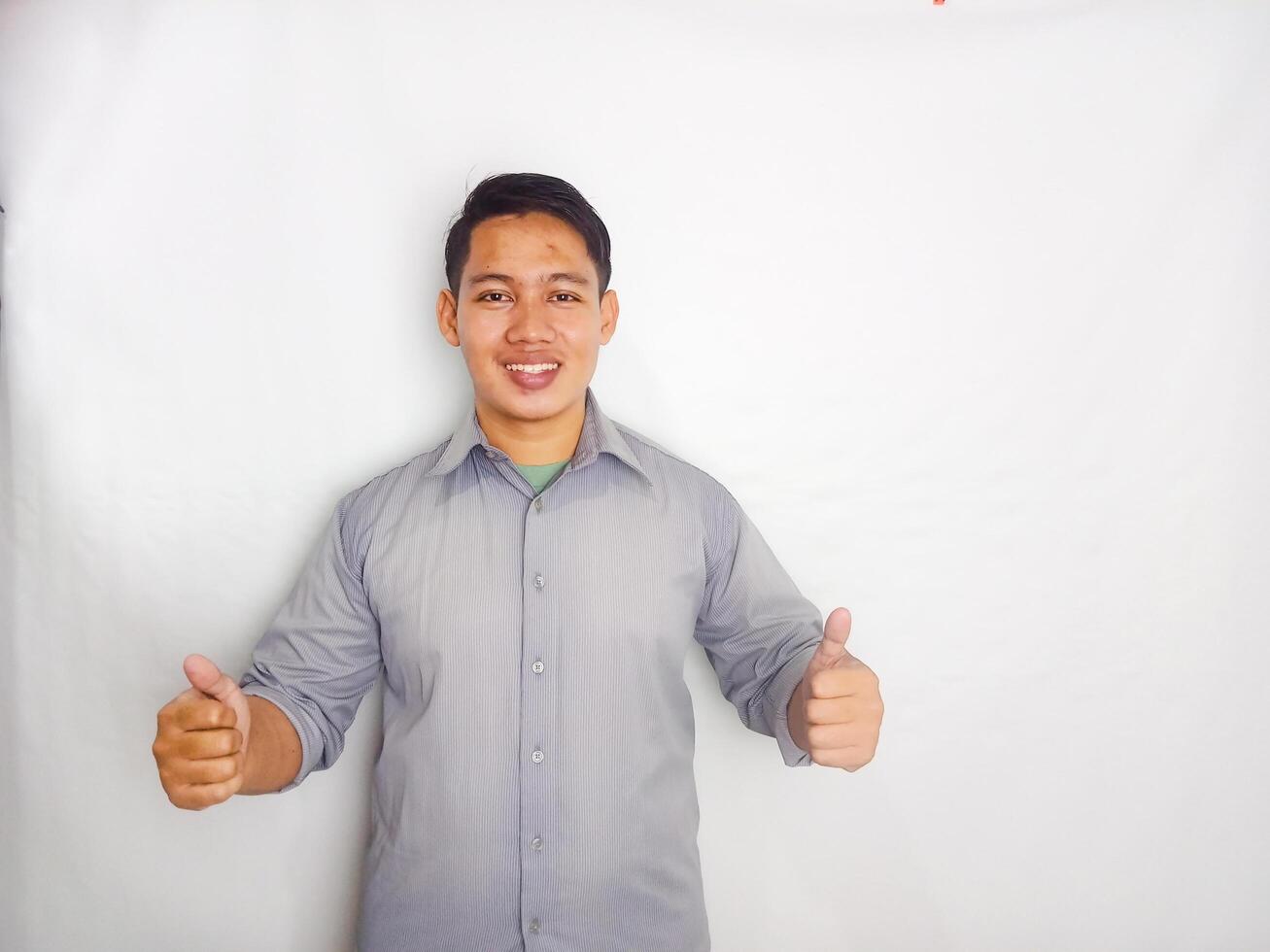 Adult Asian man smiling happy while pointing and give OK sign. wearing grey shirt isolated on white background photo