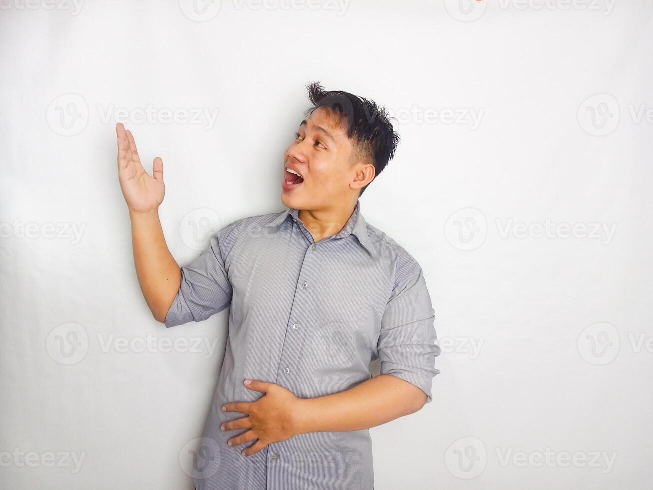 Attractive Young Asian man smiling while pointing to copy space area wearing grey shirt isolated on white background photo