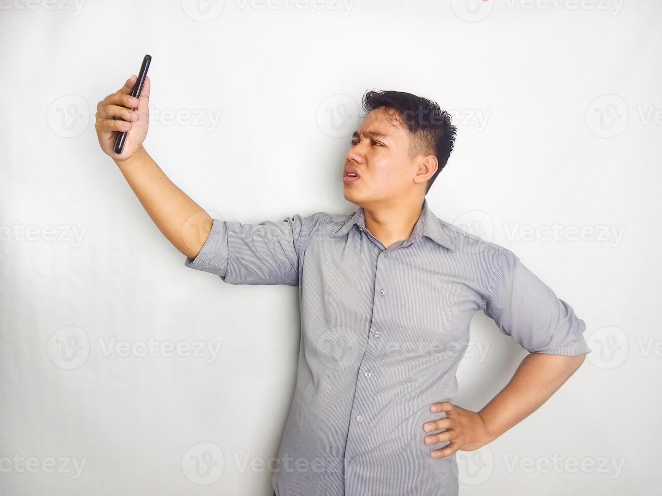 A Young man showing disappointed expression when looking to his mobile phone, wearing grey shirt isolated on white background photo