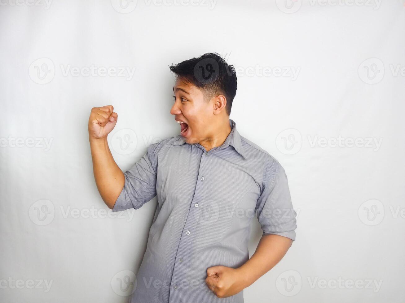 Young Asian man showing wow face expression when looking to his mobile phone wearing grey shirt isolated on white background photo