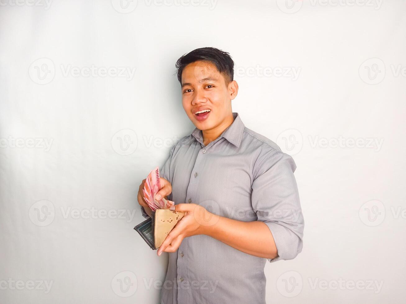 Side view of Young asian man smiling happy while taking out money from inside his wallet wearing grey shirt isolated on white background photo