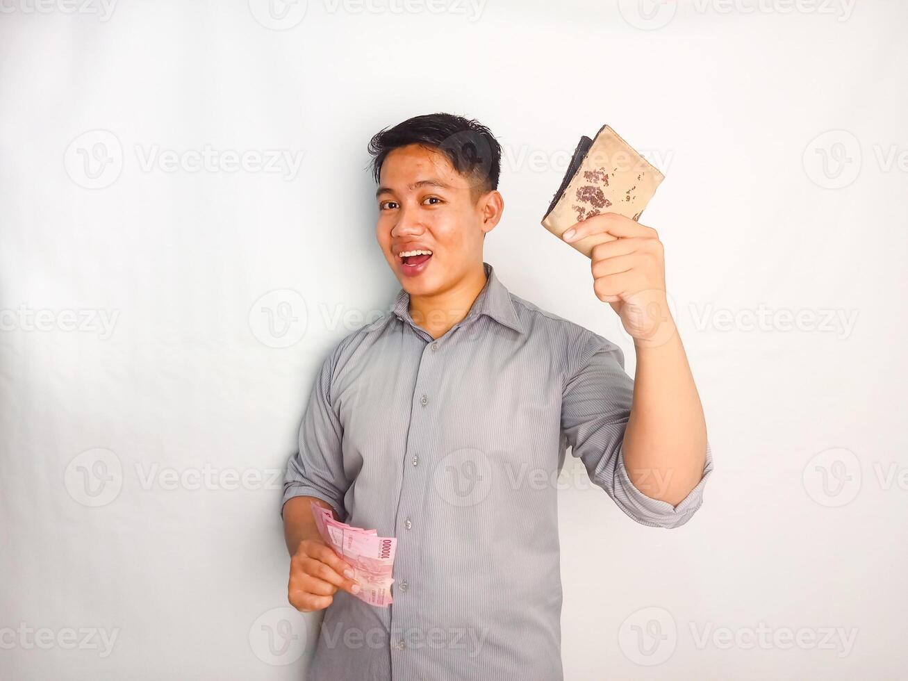 Side view of Young asian man smiling happy while taking out money from inside his wallet wearing grey shirt isolated on white background photo