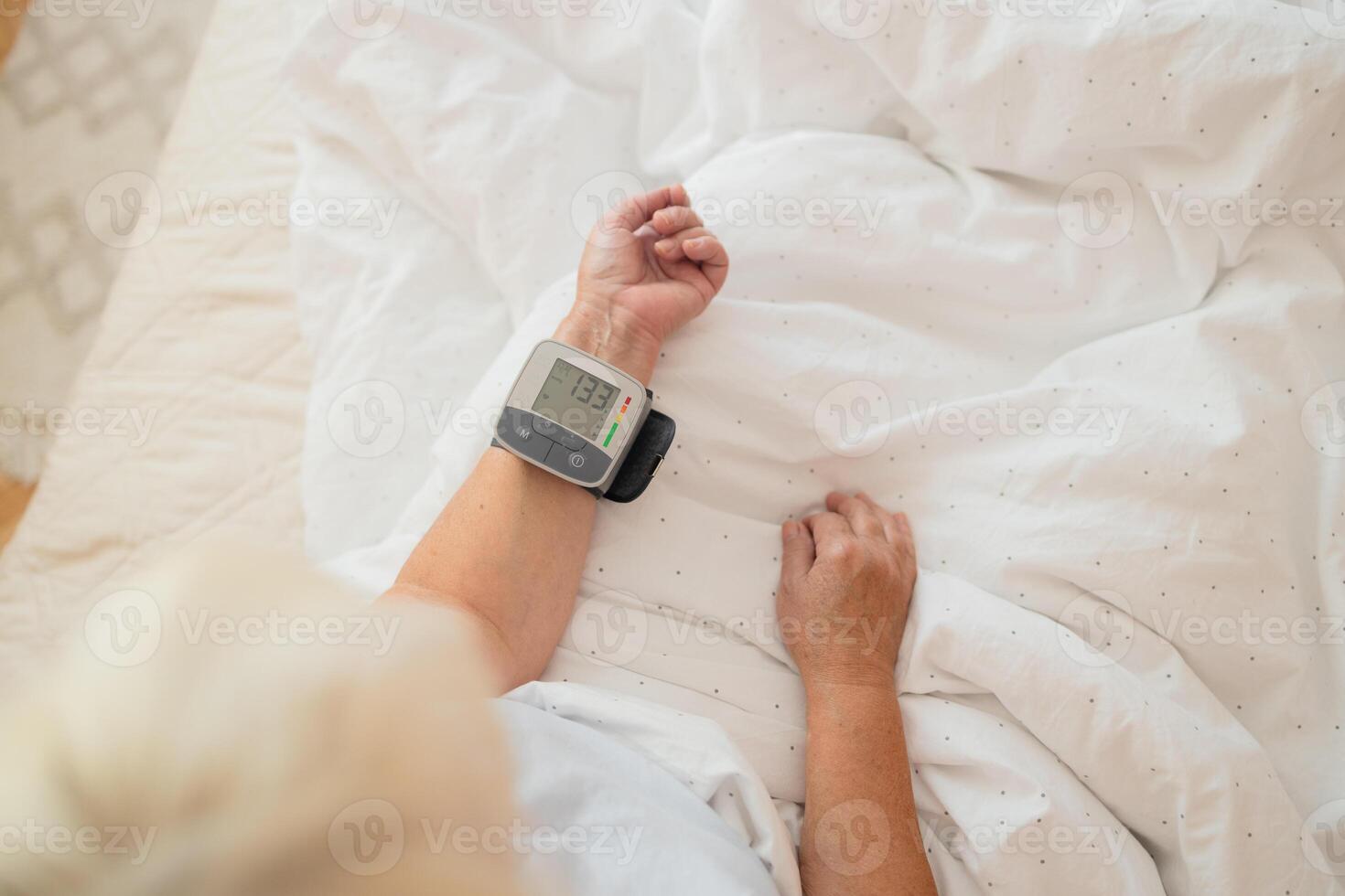 Close up of woman checks her blood pressure, a tonometer is worn on her wrist in a bed. Medical device for measuring blood pressure and heart rate used at hand wrist photo