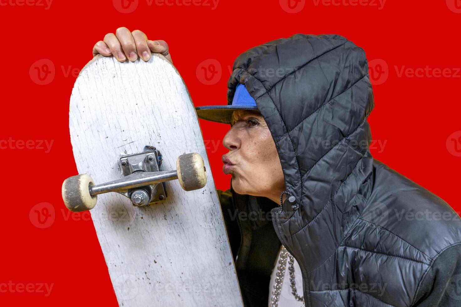 beautiful middle aged woman in black hoodie poses as rapper kissing skateboard on colorful background photo