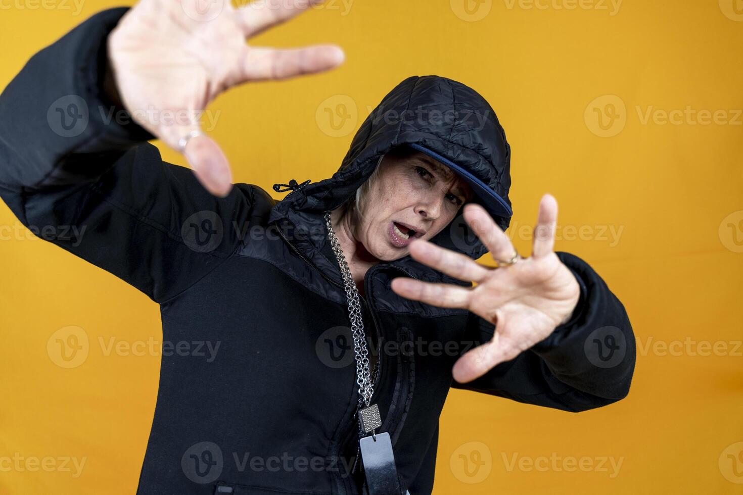 funny portrait of middle aged woman dressed as angry rapper in black tracksuit gesturing posing on colorful background photo