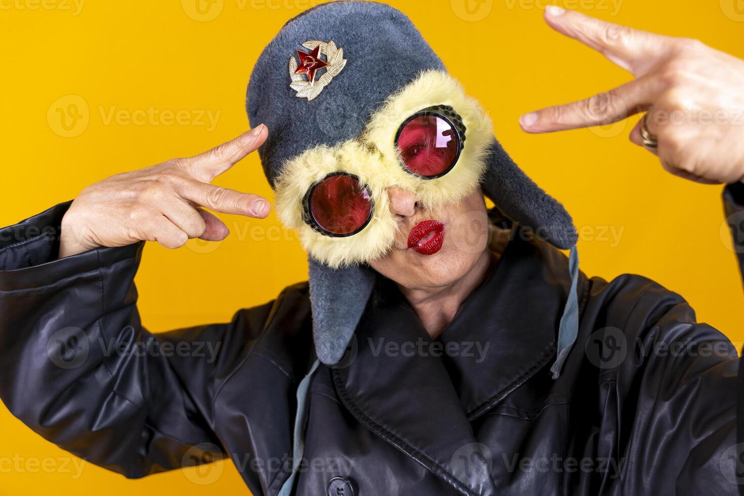 funny portrait of middle aged woman posing dressed in russian aviator leather making peace sign with hands on colorful background photo