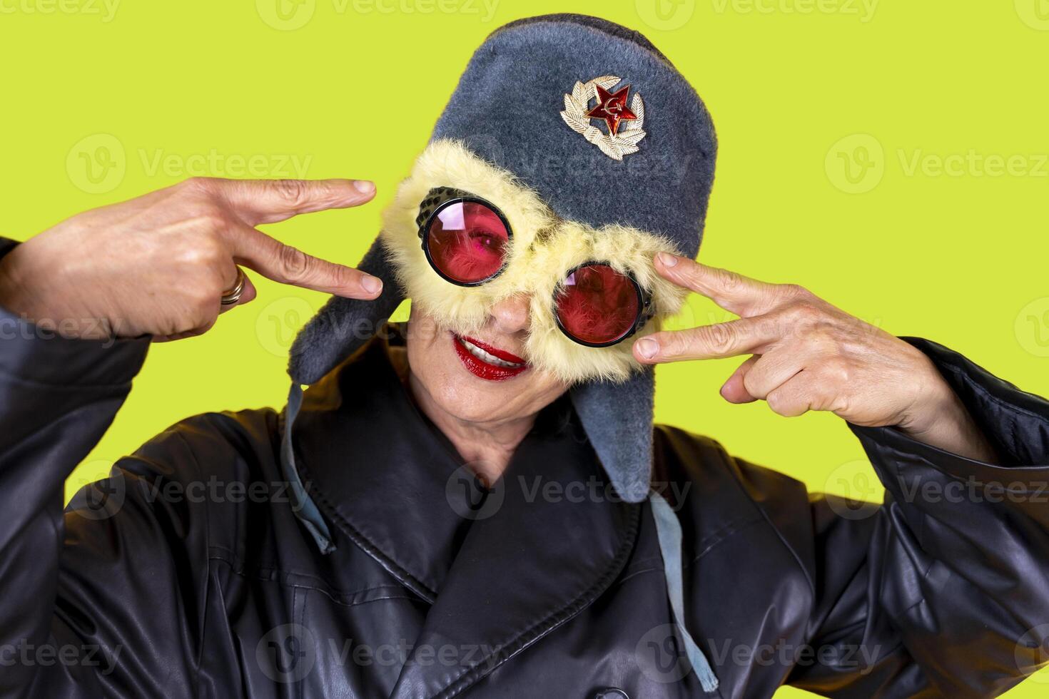 funny portrait of middle aged woman posing dressed in russian aviator leather making peace sign with hands on colorful background photo