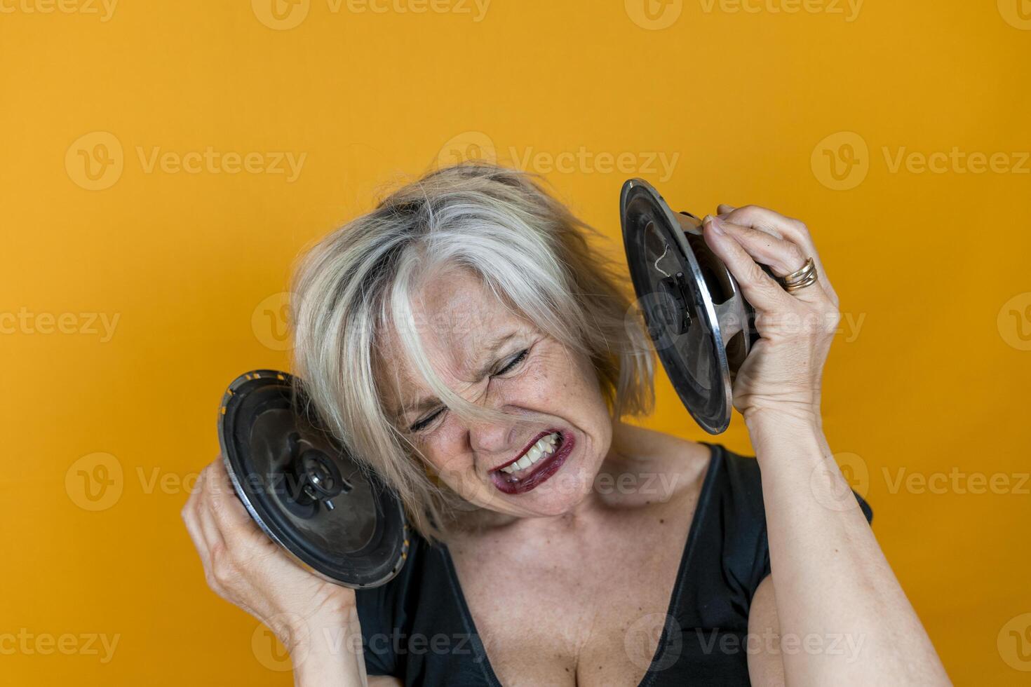 portrait of a beautifulscreaming middle-aged woman in front of a yellow background enjoying listening to loud music with speakers photo
