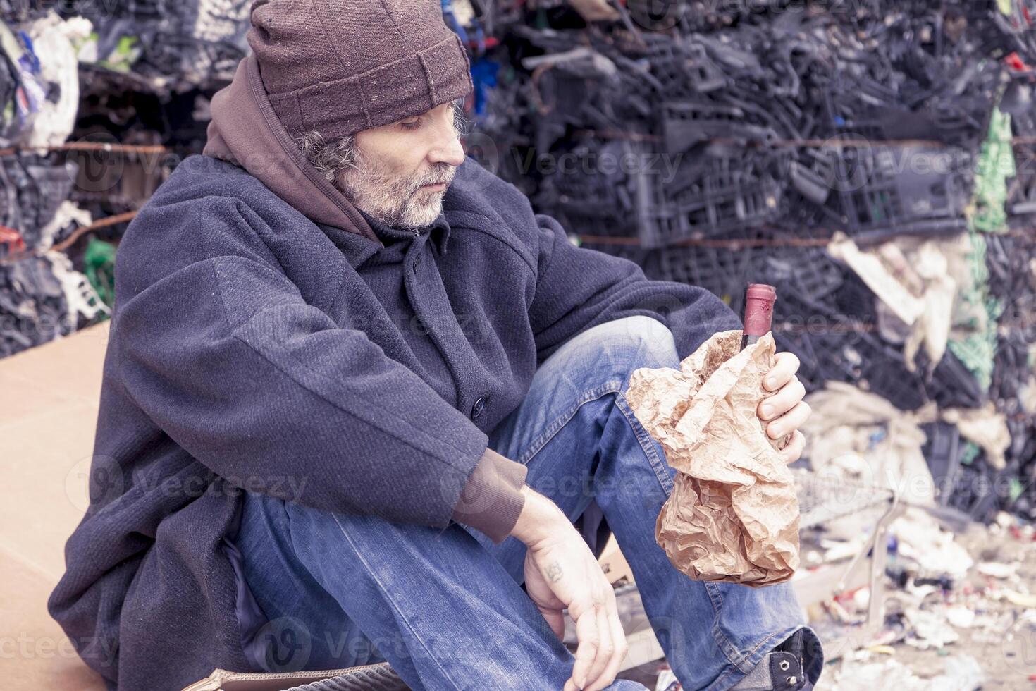 homeless man with a bottle of red wine in landfill photo