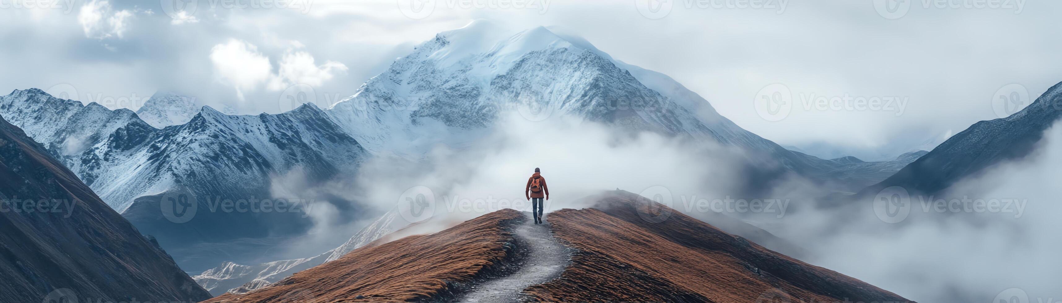 Hiker stands on a mountain trail with snow-capped peaks and clouds in the background, embracing the serene and majestic landscape. photo