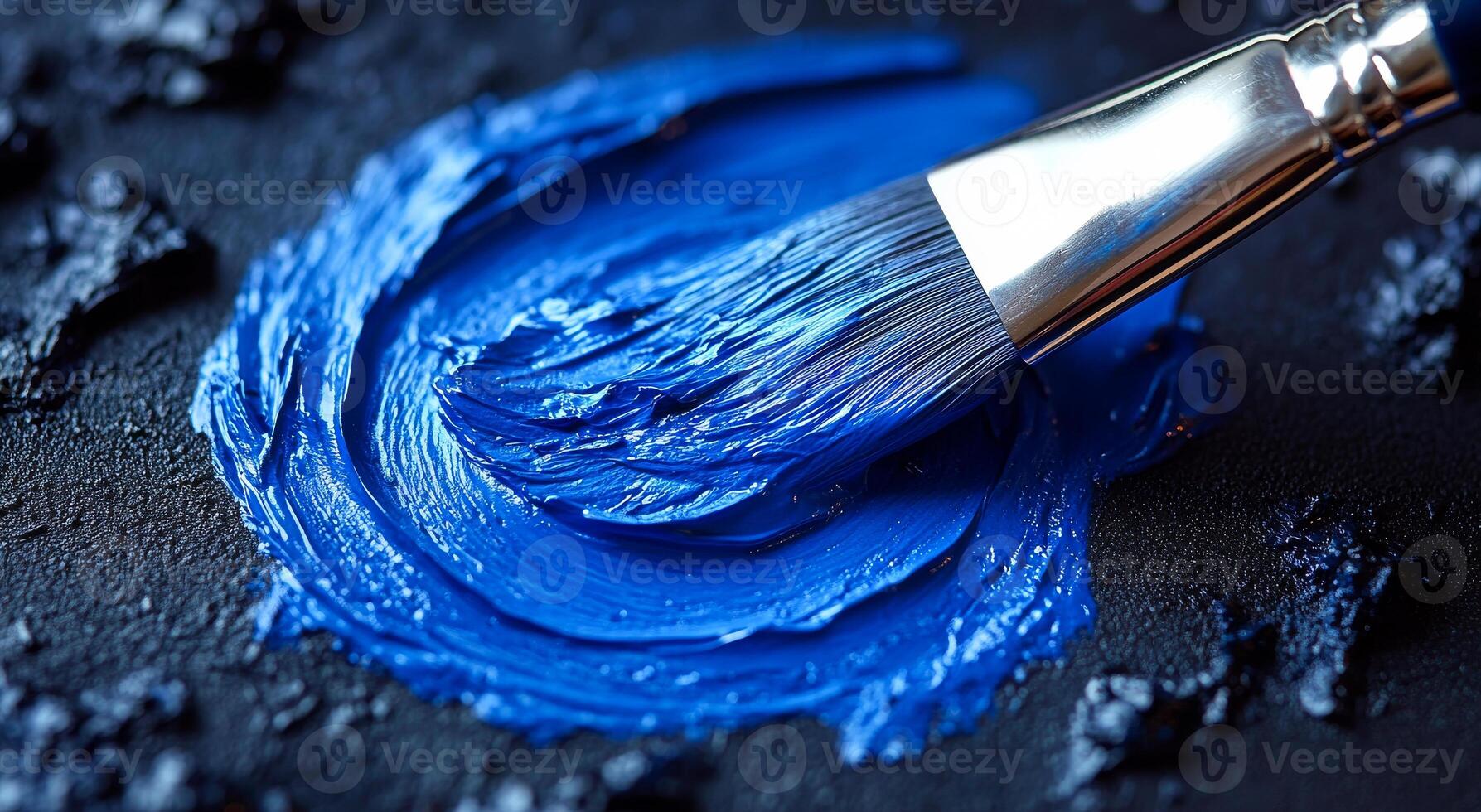 Bright blue paint applied with a brush on canvas. A vibrant blue paint is being mixed on a dark surface using a brush, showcasing the texture and color contrast vividly. photo