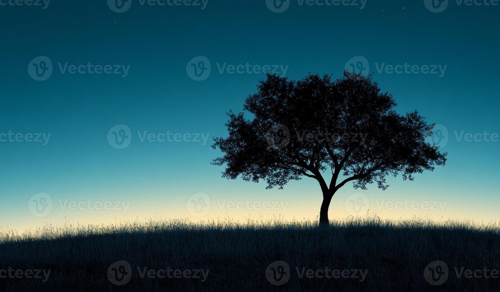 Silhouette of a solitary tree at dusk on a hilltop. A dark silhouette of a tree stands alone on a grassy hill as dusk settles, creating a serene and tranquil atmosphere. photo
