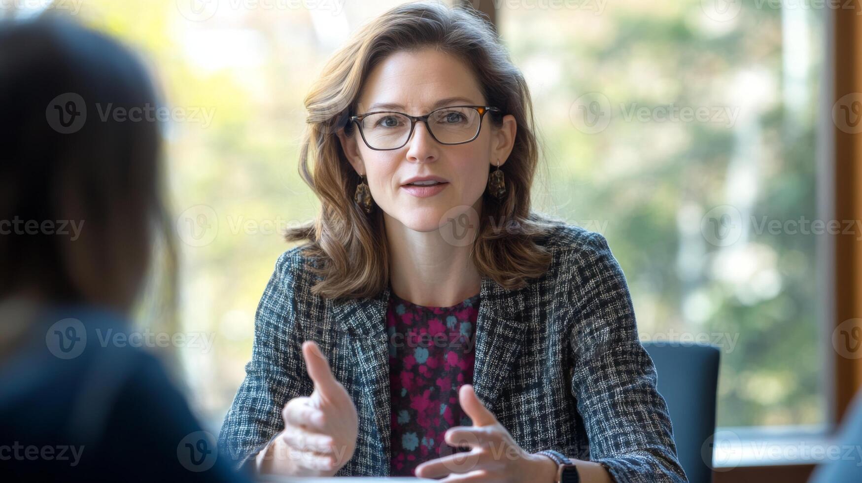 A woman with glasses and a checkered blazer gesturing during a conversation photo