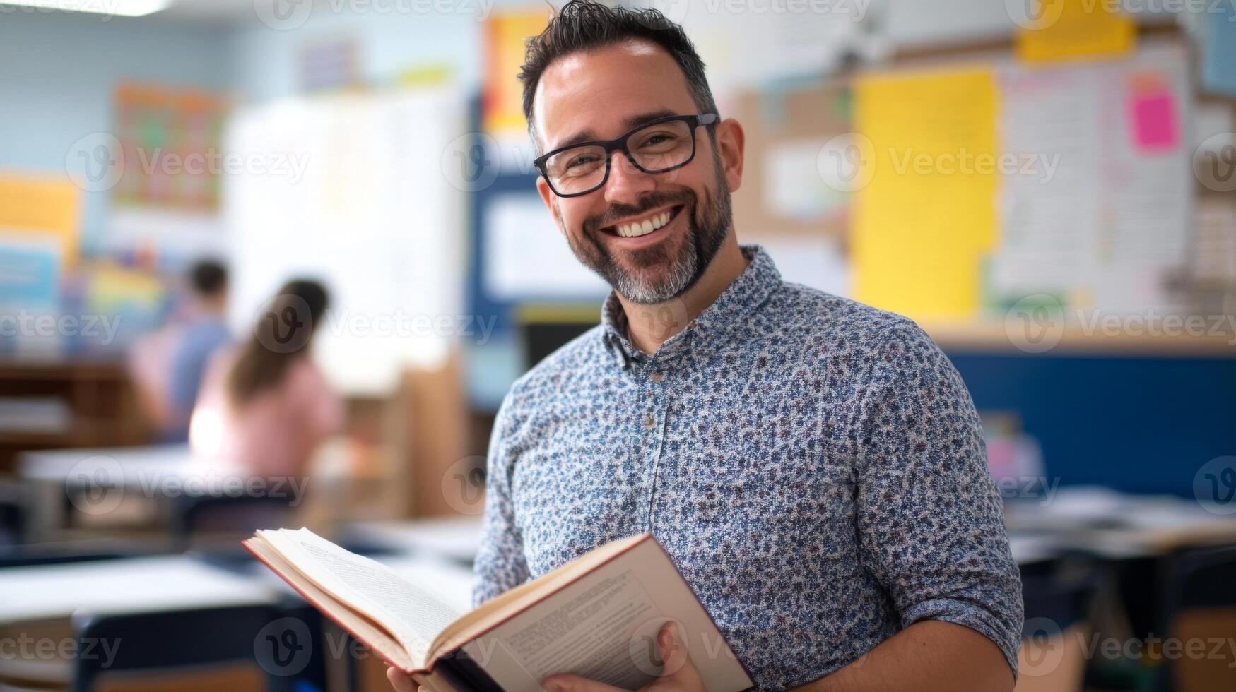 A smiling male teacher holding an open book in a classroom photo