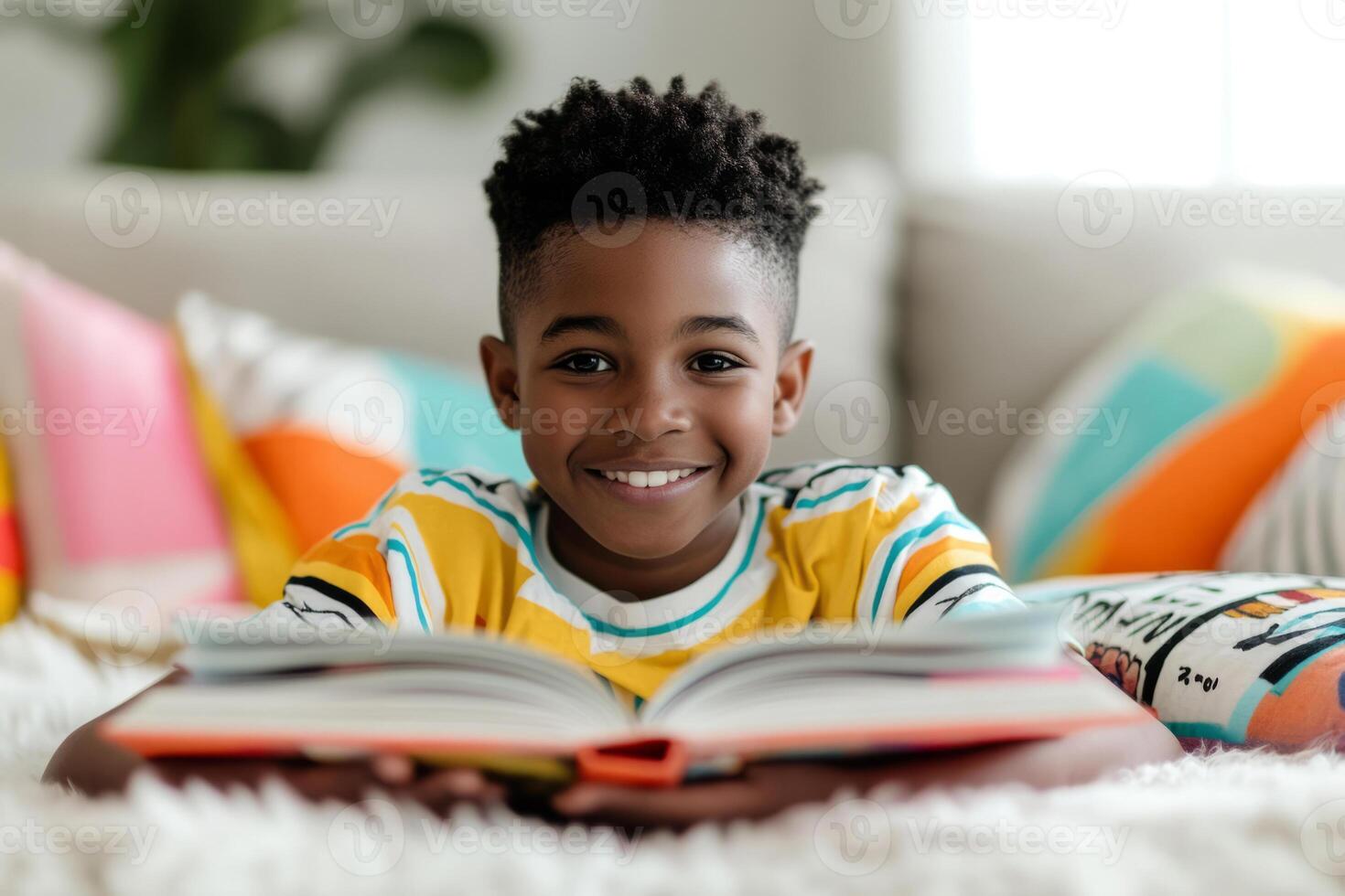 Happy young boy reading a book surrounded by colorful pillows photo