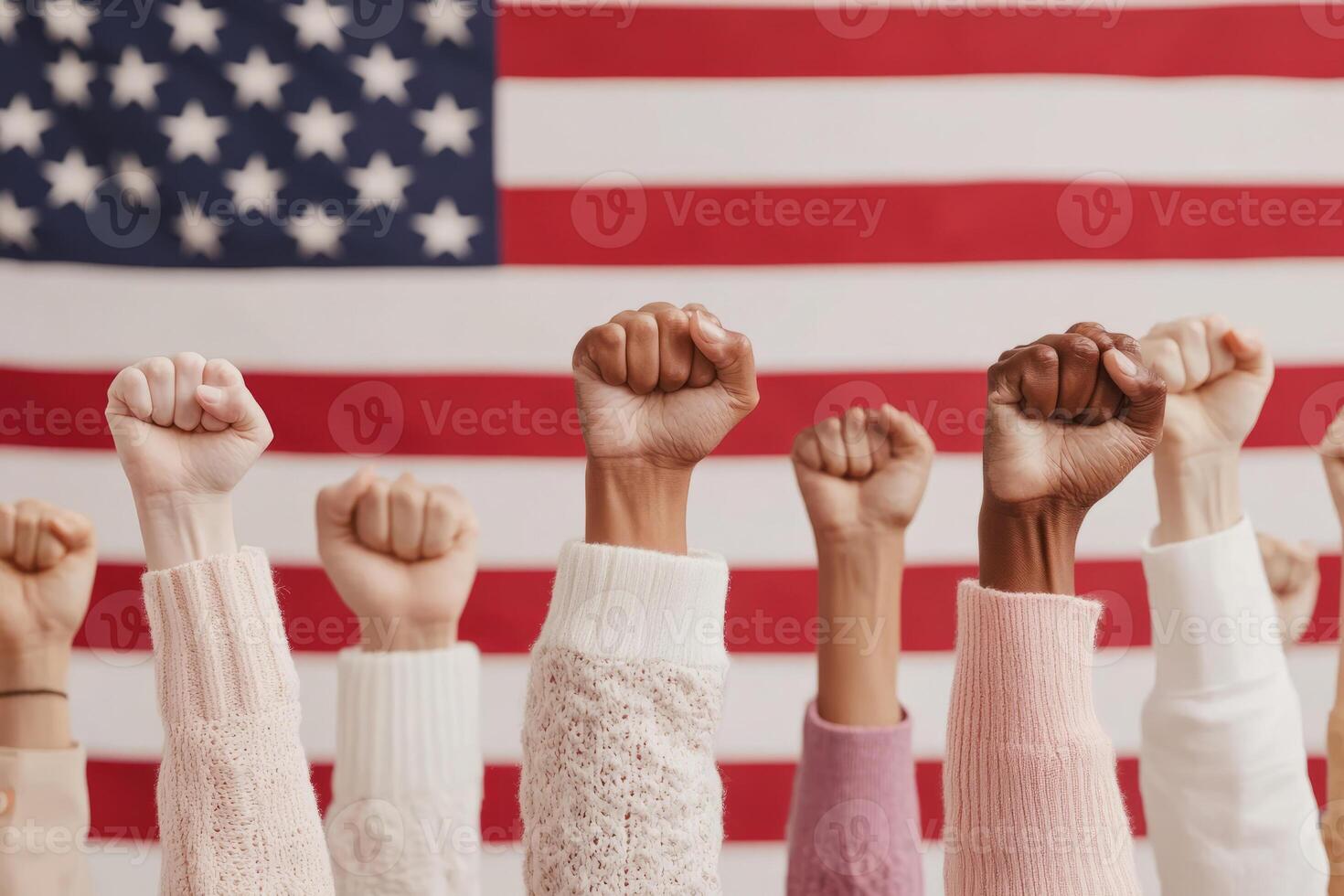 Hands with raised fists show solidarity and unity in front of a blurred American flag, symbolizing strength, activism, and diversity. photo