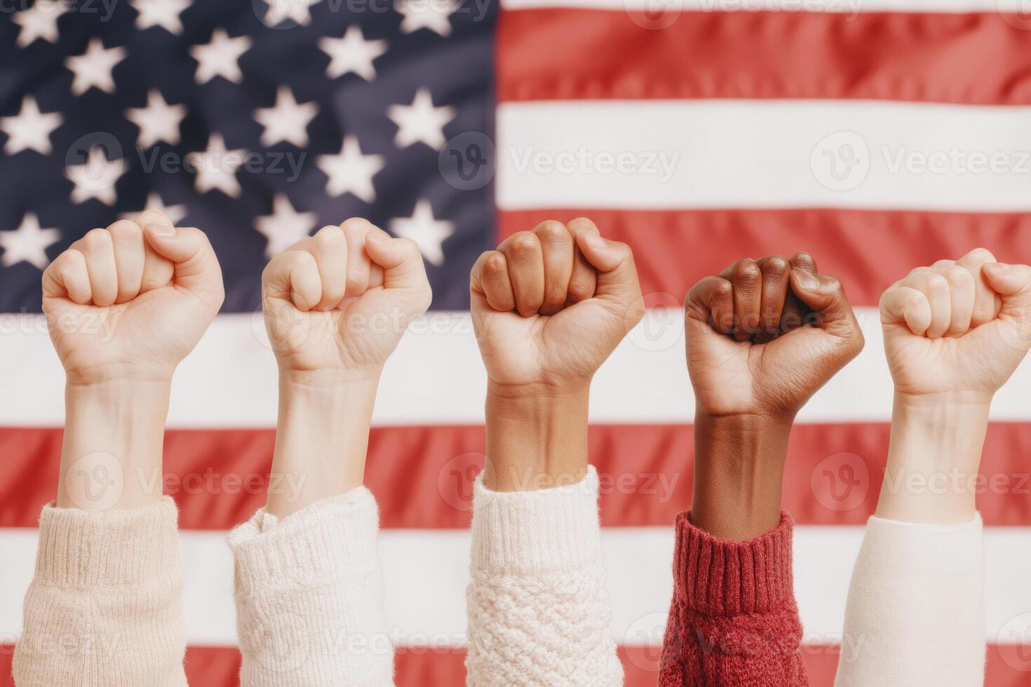 Hands with raised fists show solidarity and unity in front of a blurred American flag, symbolizing strength, activism, and diversity. photo