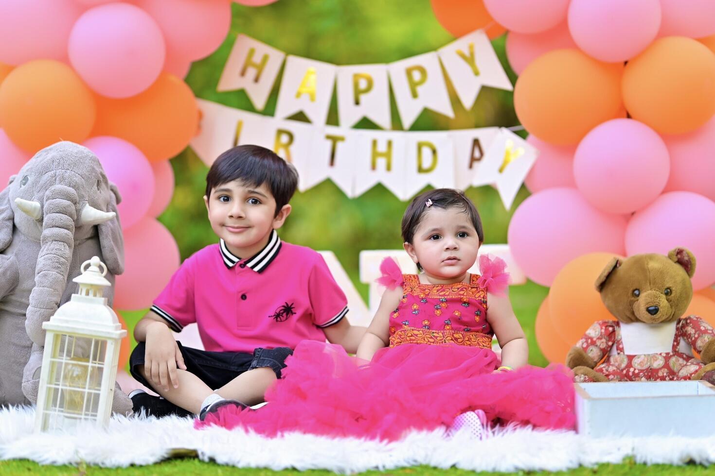 Two children in pink dresses sitting on a blanket with balloons photo