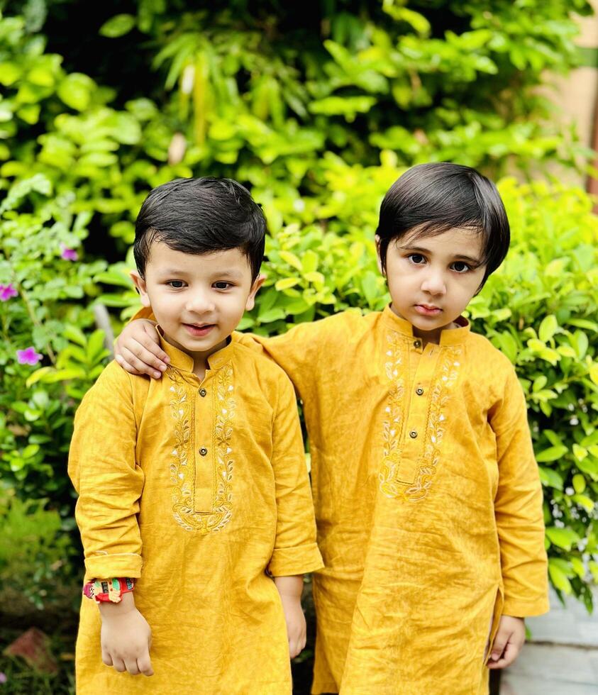 Two boys in yellow kurta and pants standing in front of a garden photo