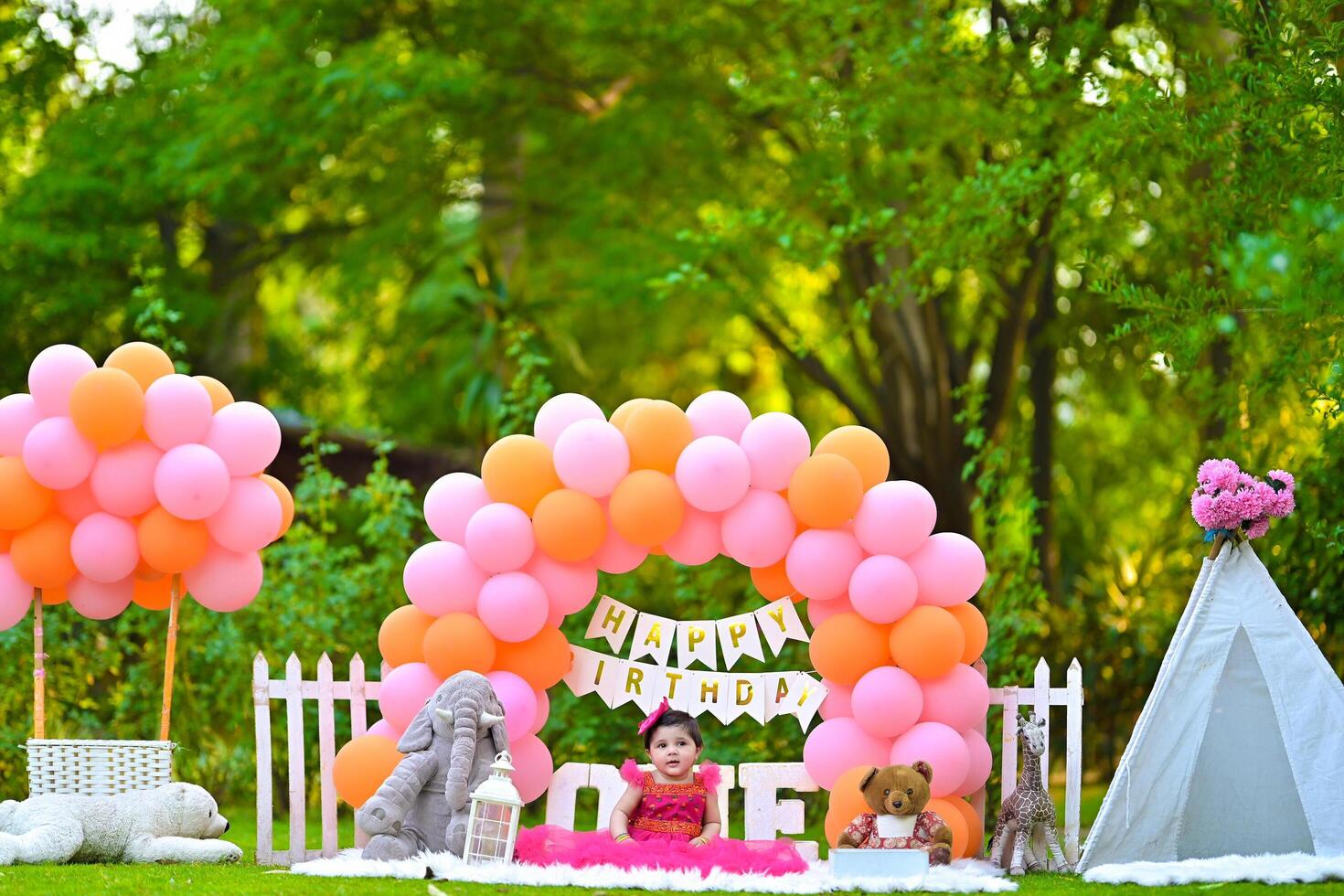 A baby girl sitting in a tent with balloons and a birthday cake photo