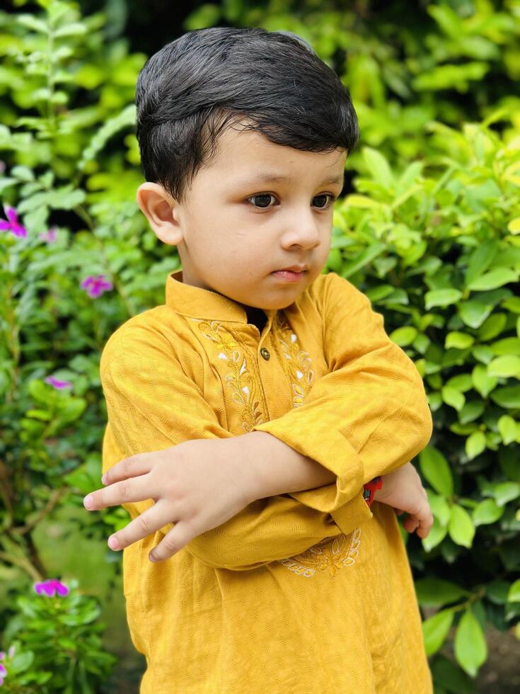 A young boy in yellow standing in front of some bushes photo