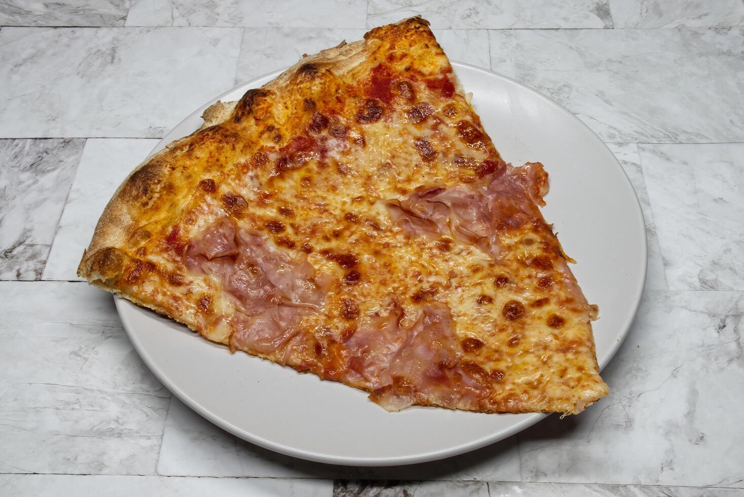 Slice of Italian pizza with ham and mozzarella in a white dish. photo