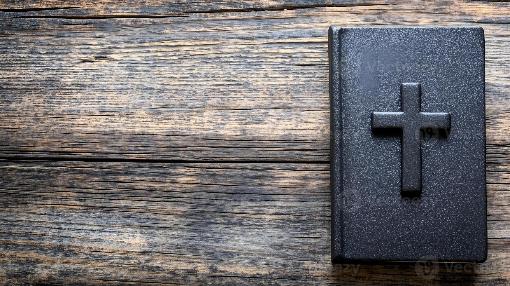 A cross resting on a black book placed on a rustic wooden background with space photo
