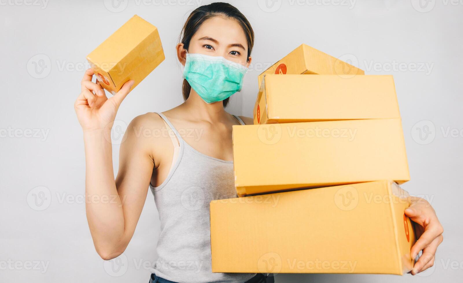 Asian woman wearing mask and holding parcel boxes for delivery. The COVID-19 outbreak, has had a positive impact on the e-commerce sector as the virus has created a new normal in online shopping. photo
