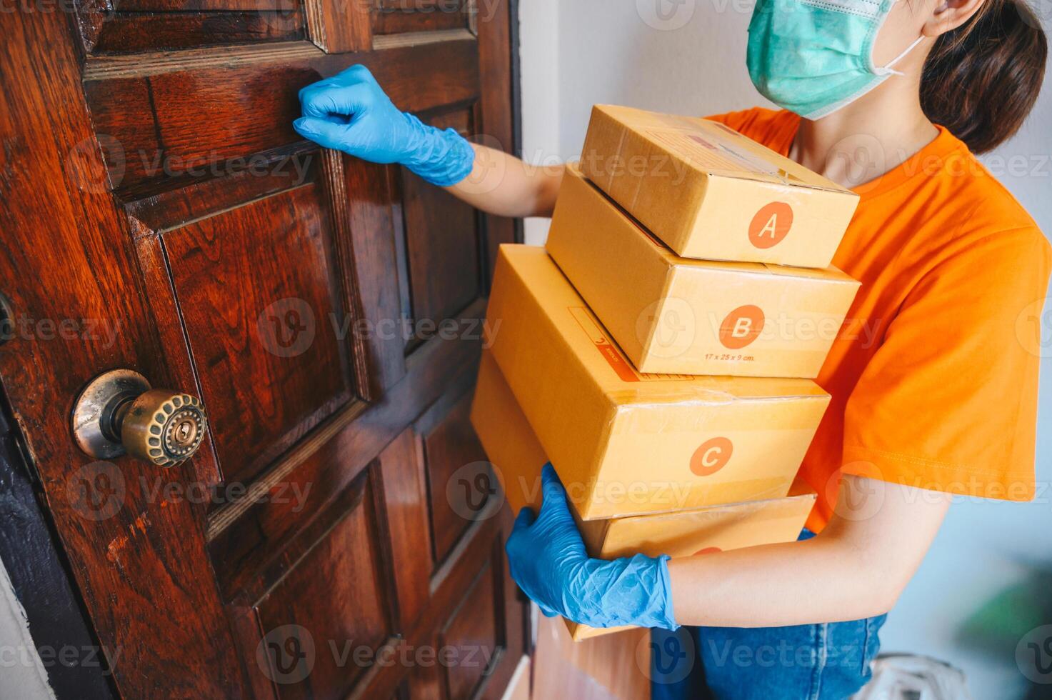Delivery service courier knocking the house door with boxes in her hands while wearing mask and glove for protect herself in covid-19 pandemic outbreak. photo