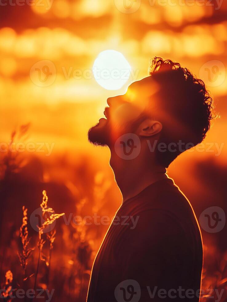 A person prays at sunset, silhouetted against a golden sky with tall grass in the foreground photo
