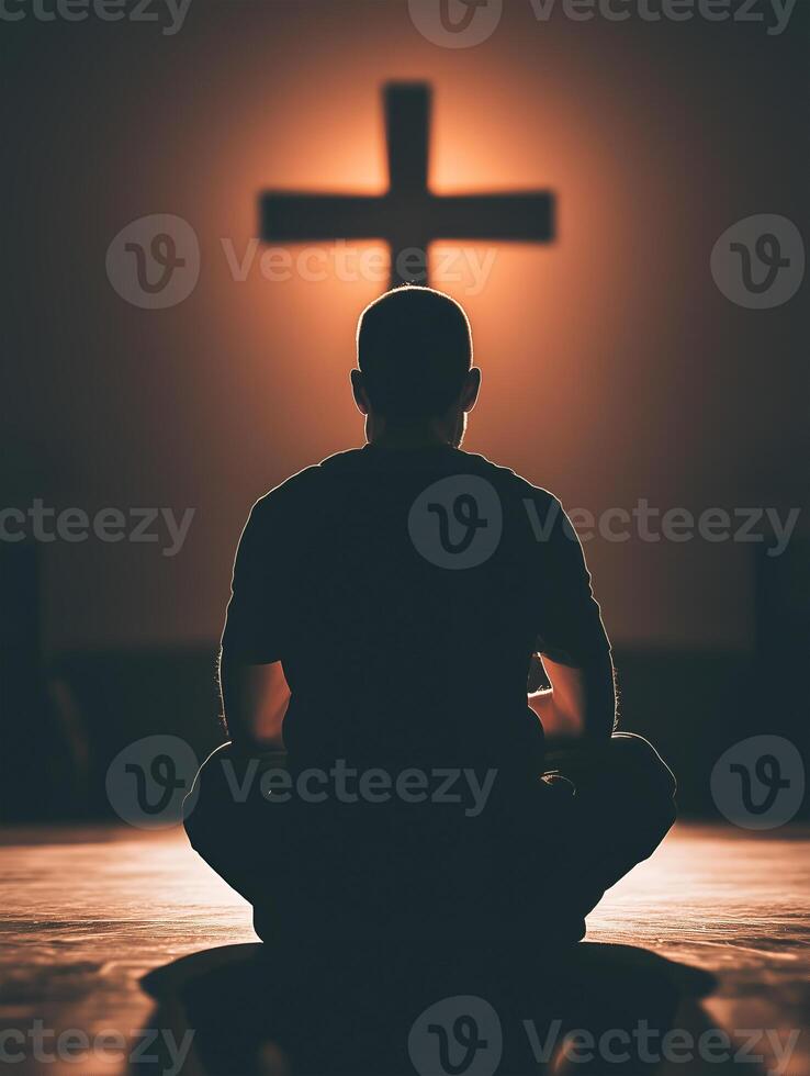 A priest in quiet prayer under a glowing cross during evening worship service indoors photo