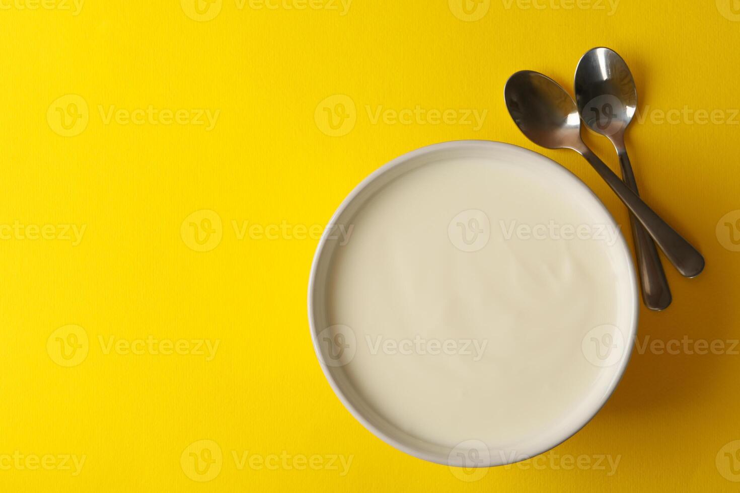 Bowl of sour cream yogurt and spoons on yellow background photo