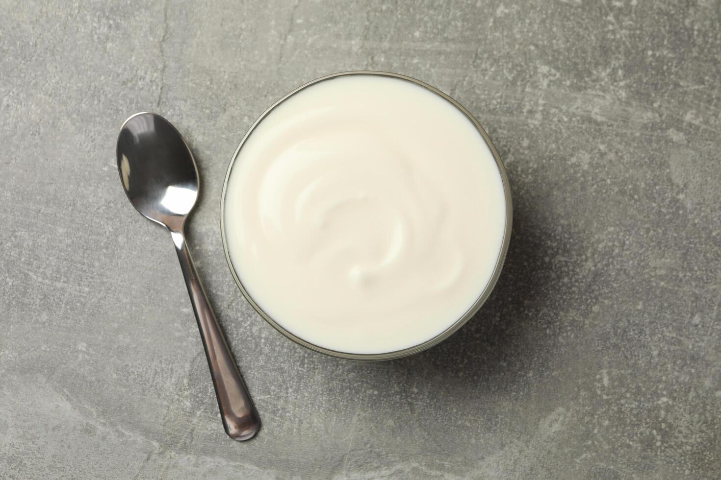 Spoon and bowl of sour cream on gray background, top view photo