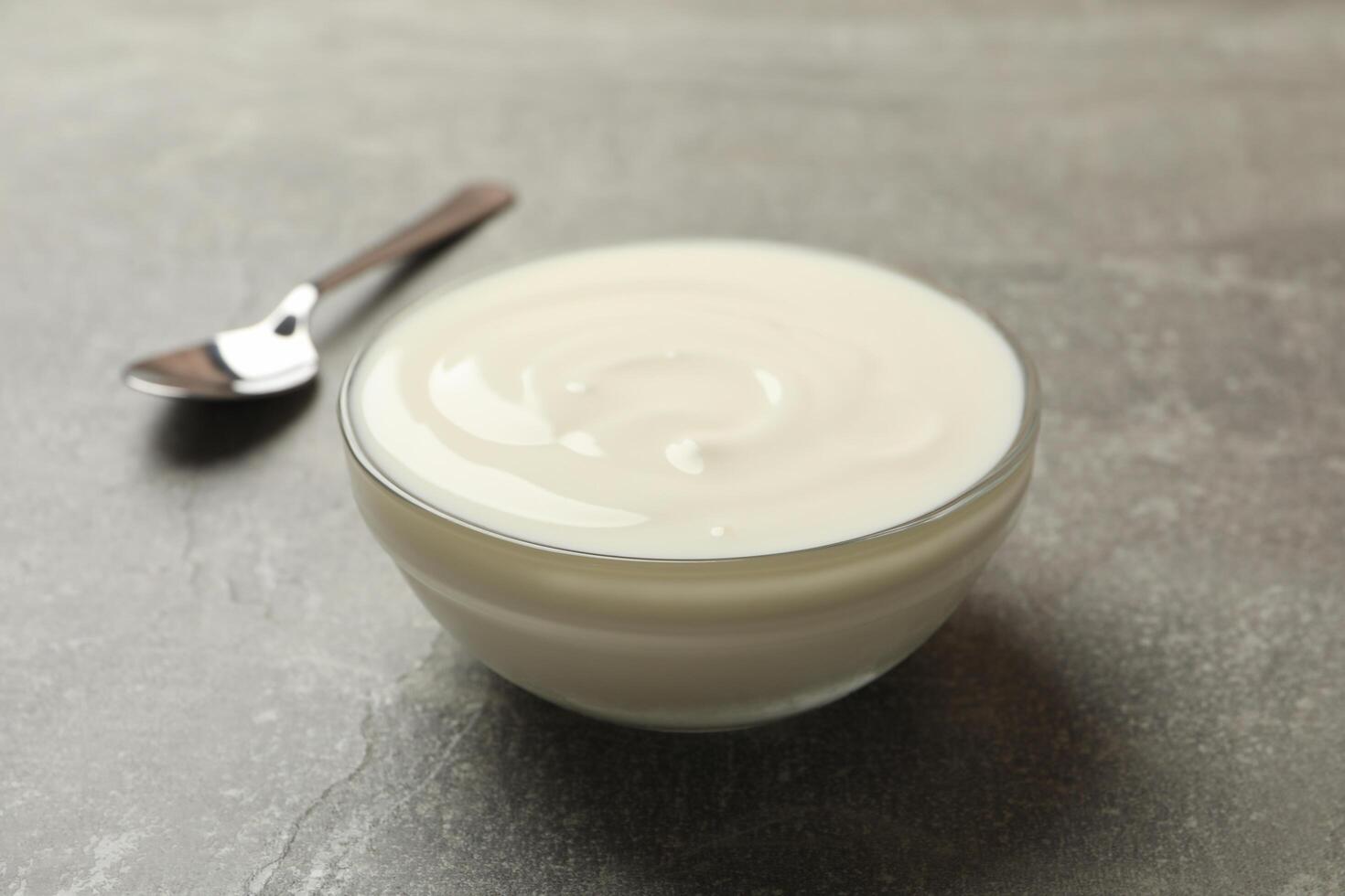 Spoon and bowl of sour cream on gray background, close up photo
