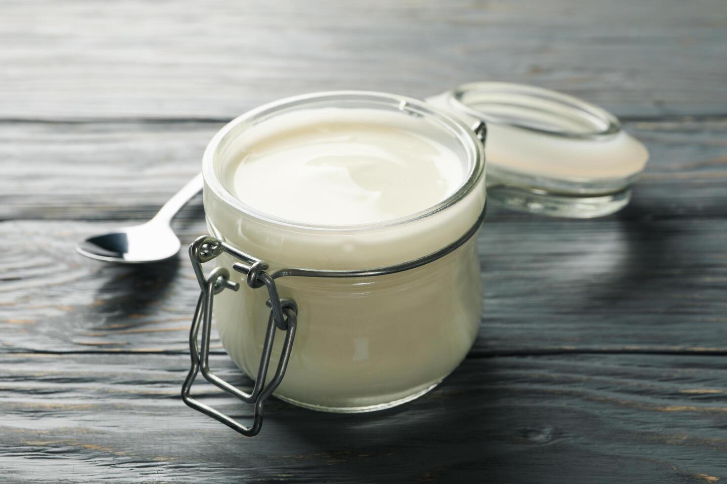 Glass jar of sour cream yogurt and spoon on gray wooden background photo
