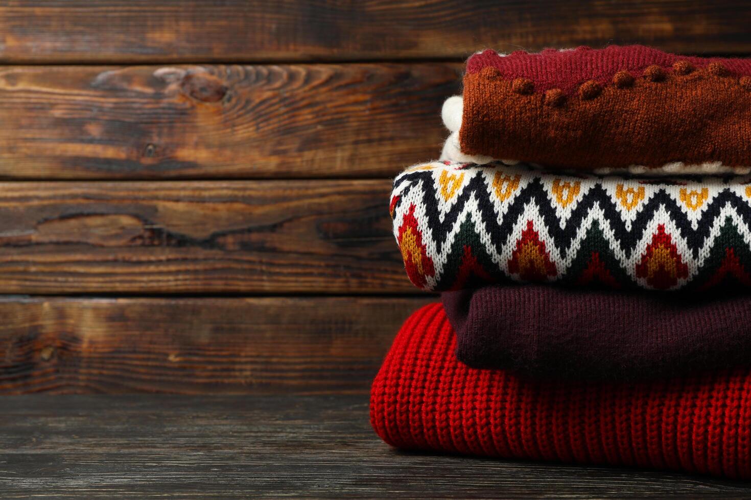 Pile of sweaters on wooden background, space for text photo