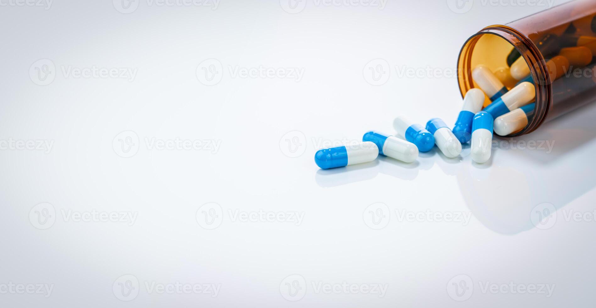 Prescription antibiotic capsules spilling from amber bottle on white background. Blue and white capsule pills. Healthcare and pharmaceutical. Medical treatment pills. Pharmacy and medicine industry. photo