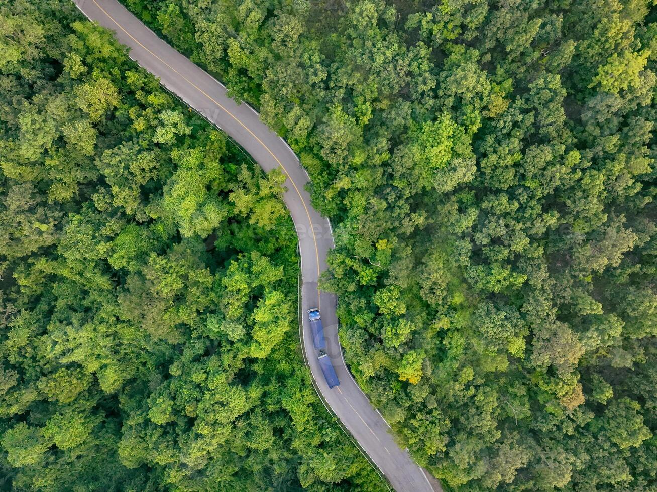 Aerial view hydrogen truck on forest highway. Sustainable transportation. Blue zero emission vehicle driving through green landscape. Eco-friendly logistics solution. Clean energy freight delivery. photo