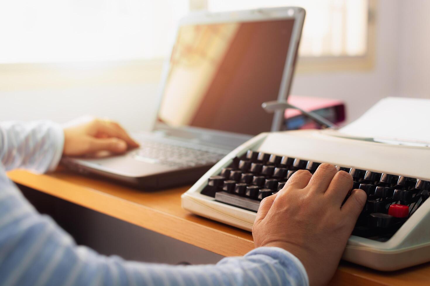 Woman typing both typewriter and laptop on working desk in office. photo