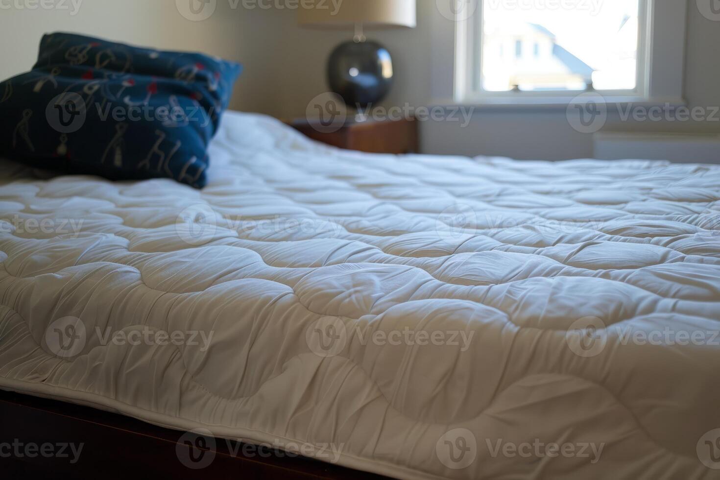 Empty bed with white duvet and blue pillow in bedroom photo