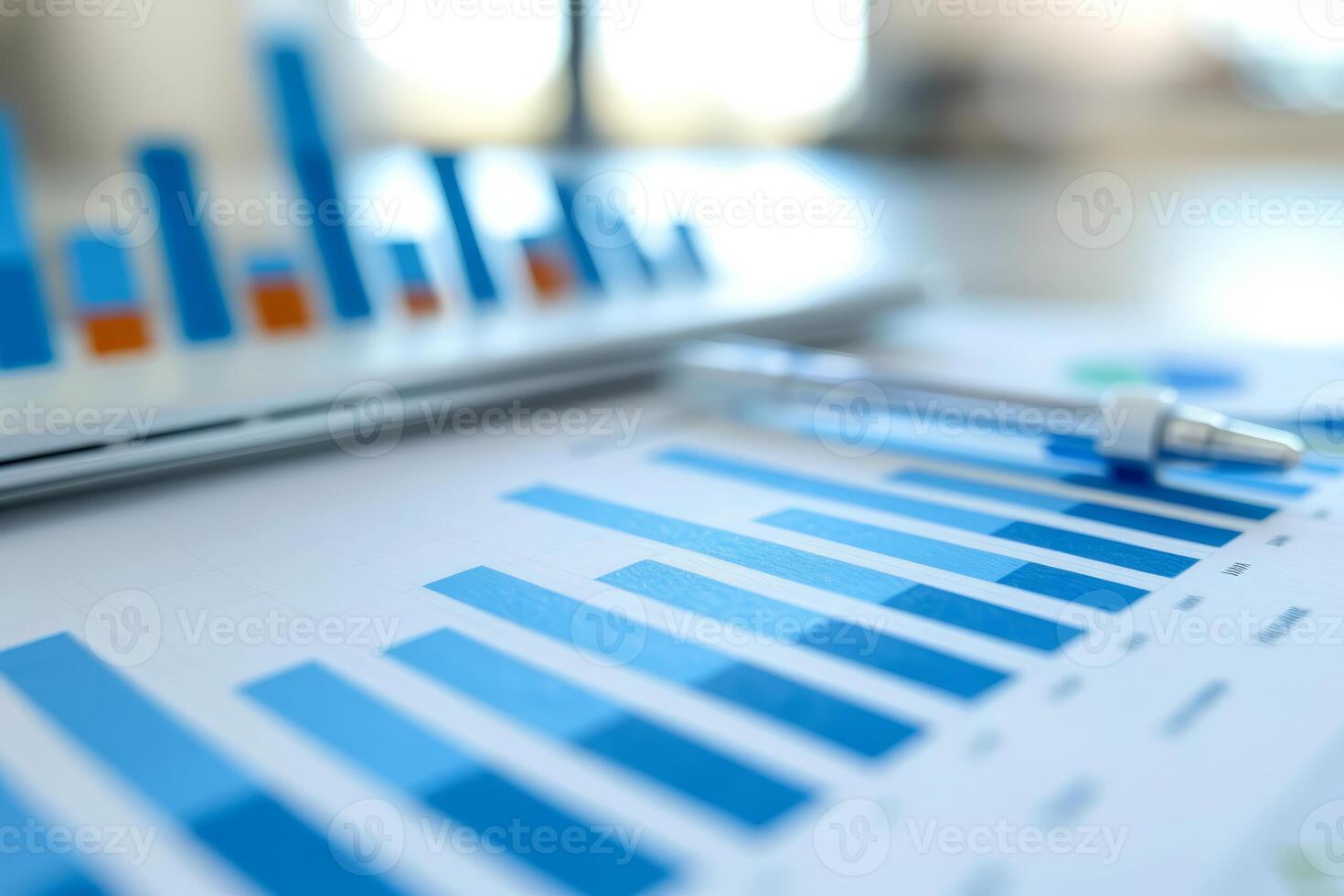 Silver pen lying on desk in front of charts and laptop showing business growth photo