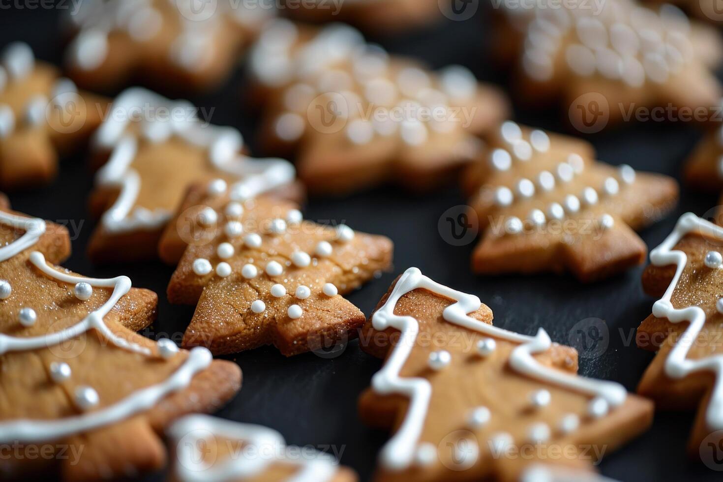 Christmas tree shaped gingerbread cookies covered in white icing and sprinkles resting on black surface photo