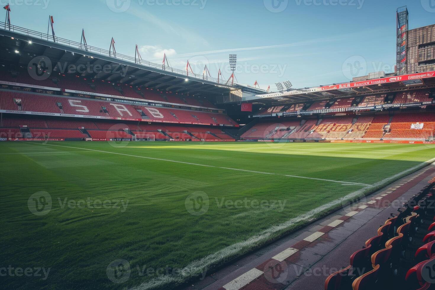 Empty soccer field inside stadium with red seats under blue sky photo
