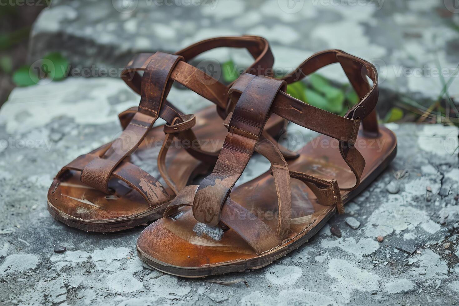 Pair of worn brown leather sandals resting on concrete block photo