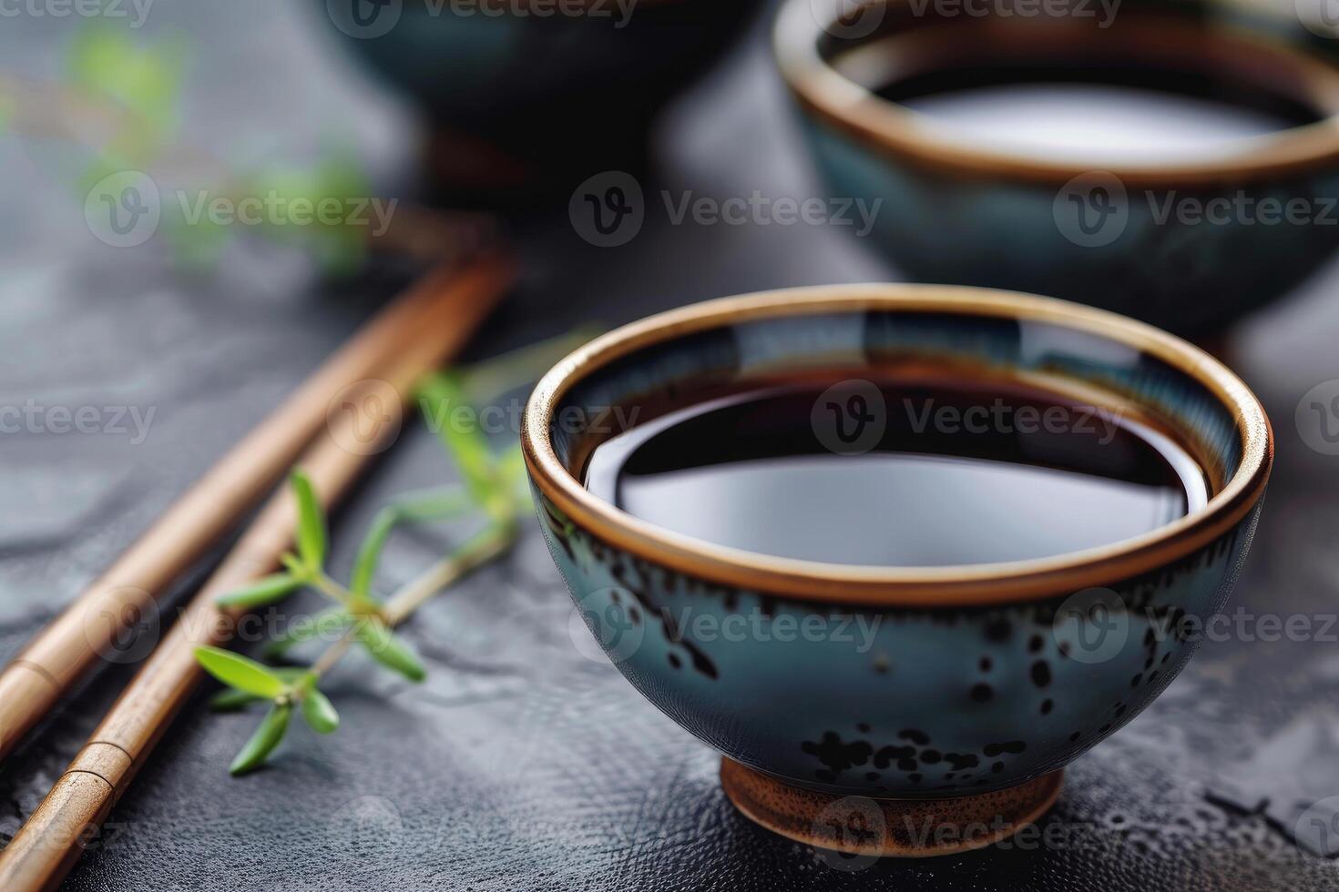Bowls filled with soy sauce resting on dark surface with chopsticks photo