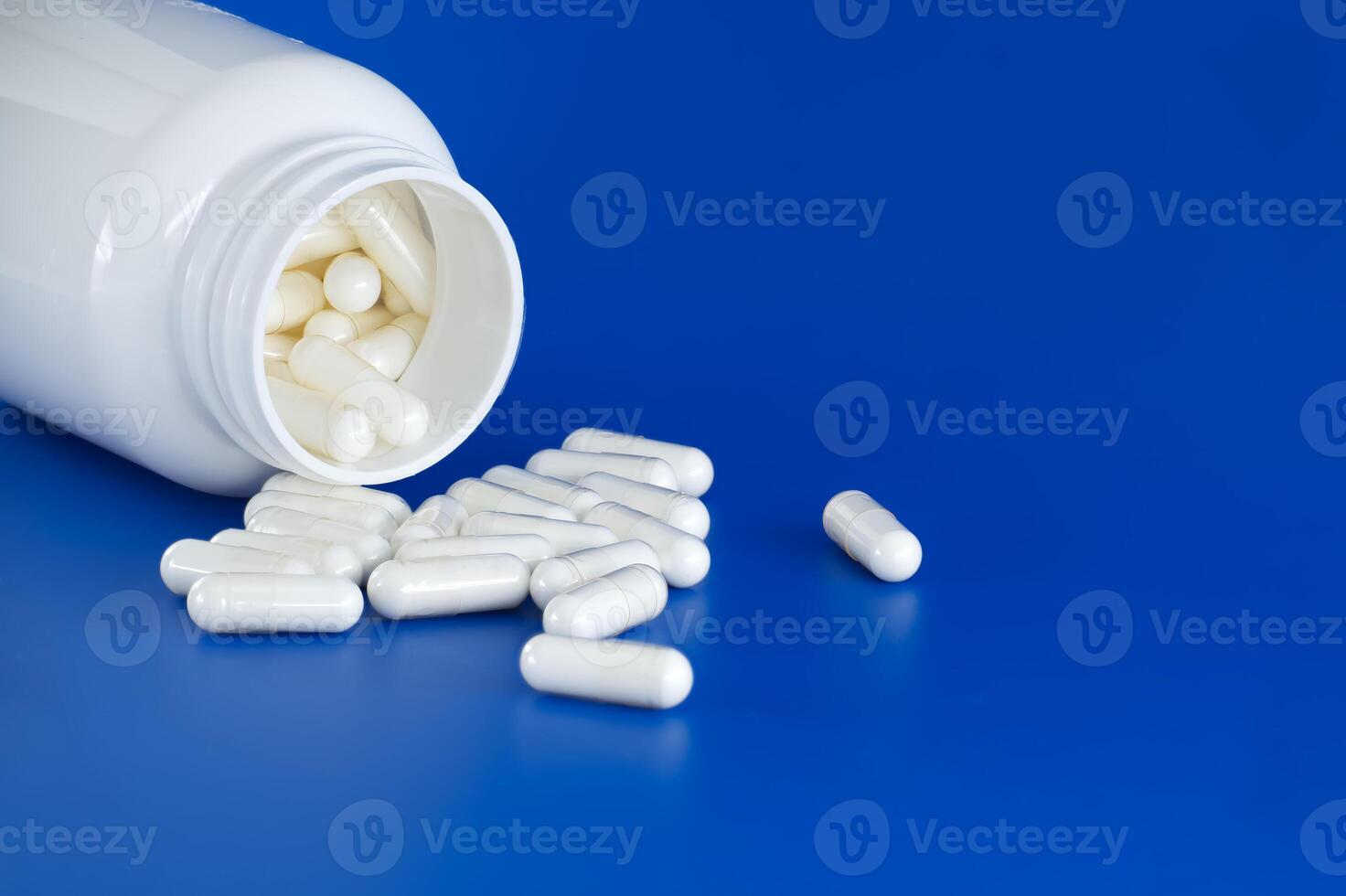 White medicine bottle spills pills over blue background photo