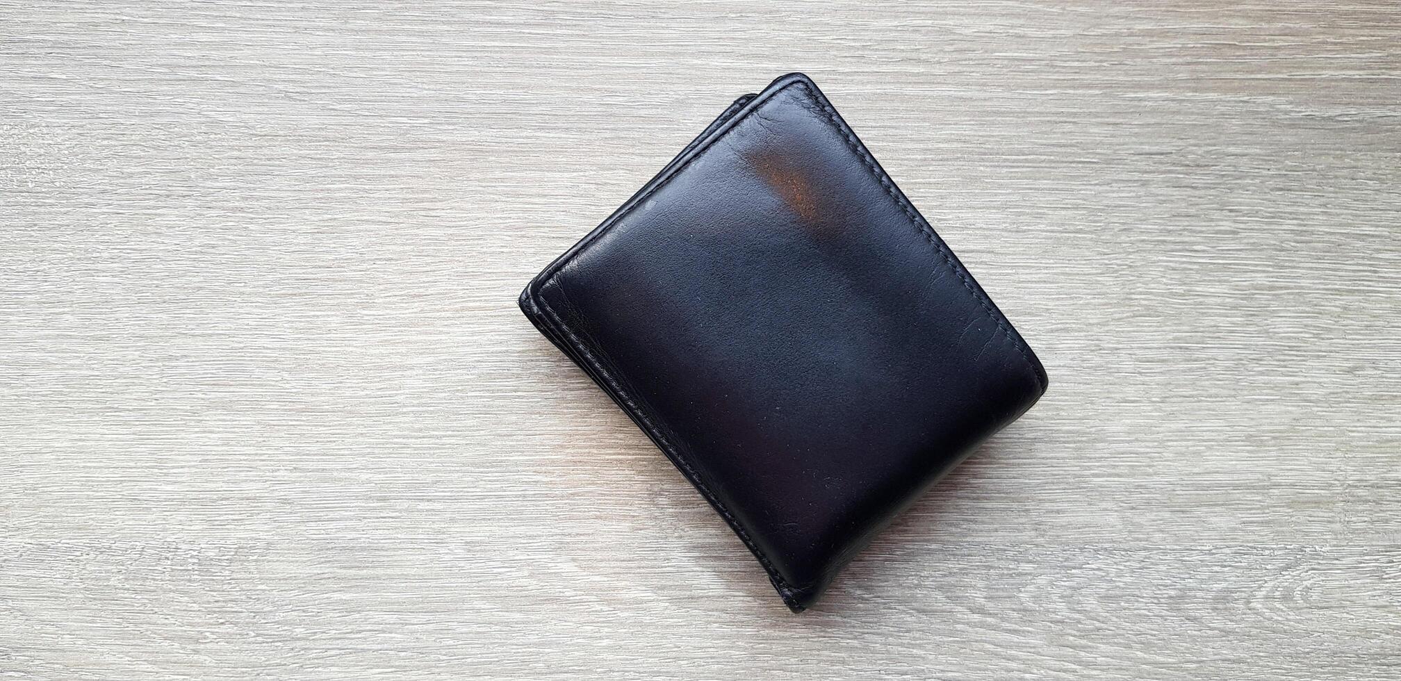 Black or brown leather wallet on light brown wooden table or background with copy space. Object, Money and Shape concept. photo